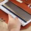 A hand is placing a silver tablet into a leather document organizer bag alongside A4 files.