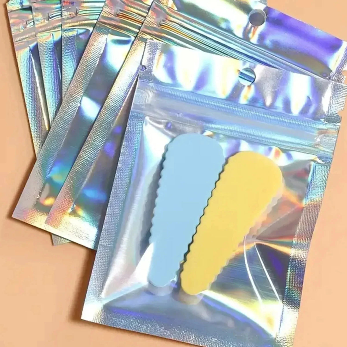A stack of holographic rainbow pattern sealing bags containing blue and yellow stickers.