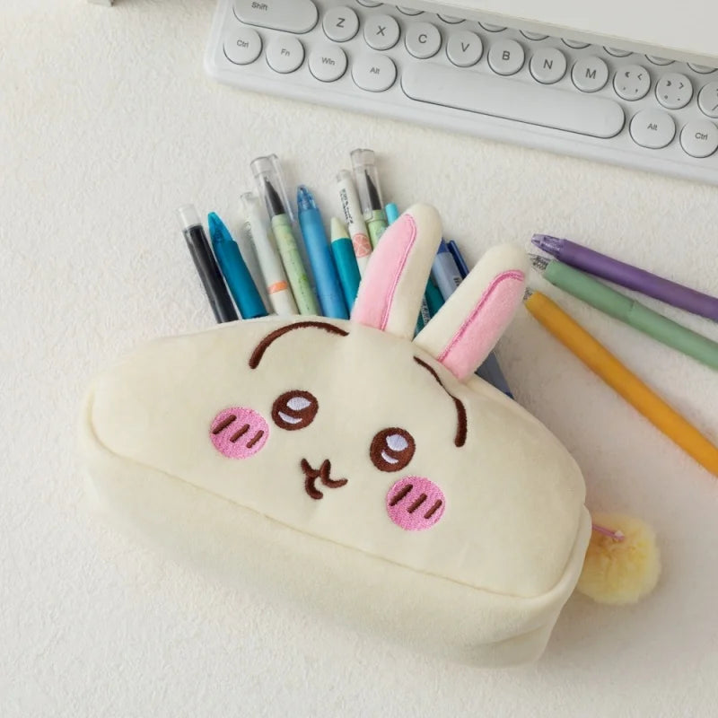 A cute white Chiikawa plush pencil case shaped like a rabbit, resting on a white surface next to colored pencils.