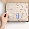 A hand is holding a kraft paper box filled with thank you stickers featuring minimalist line art faces.