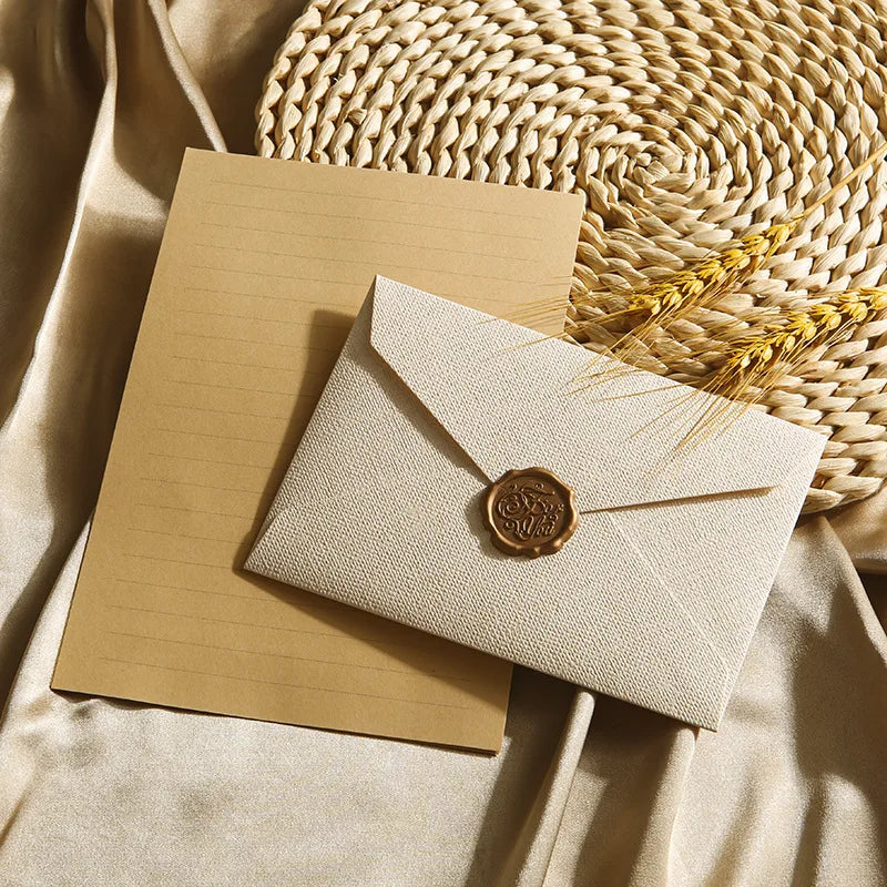 Beige Leinenumschlag und Briefset mit Wachssiegel auf hellem Tanpapier neben geflochtenem Stroh.