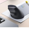 A black ergonomic vertical wireless mouse is shown resting on a white sheet of paper next to a silver laptop.
