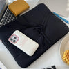 A black padded sleeve case holding a white electronic device, placed on a white surface next to a laptop.