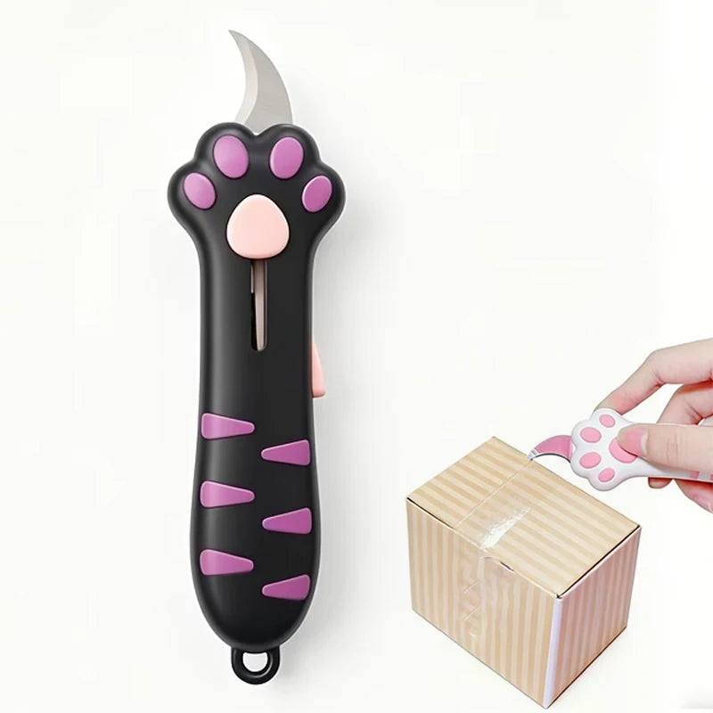 A black utility knife shaped like a cat paw with pink accents, resting next to its packaging box.
