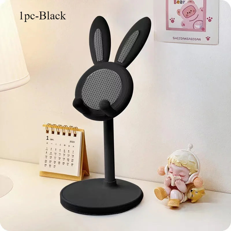 A black rabbit-shaped phone stand with long ears sitting on a white surface next to a calendar and a small plush toy.
