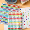 A sheet of colorful glitter foil star stickers for crafts and rewards is shown next to a spiral notebook.
