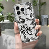 A hand holds a clear phone case with a black floral pattern and multiple camera lenses.