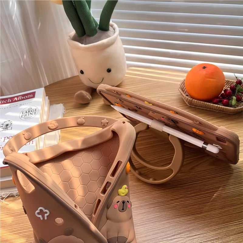 Braunes Silikon-Schutzetui für ein iPad Pro auf einem Holztisch neben einer Pflanze und einer Orange
