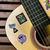 Close-up of a guitar body featuring several stickers of psychedelic aliens and leaves