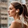 A woman wearing white athletic clothing is shown outdoors in the rain, using true wireless earbuds.