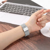 A close-up of a stainless steel Milanese loop watch band on a wrist next to a laptop.