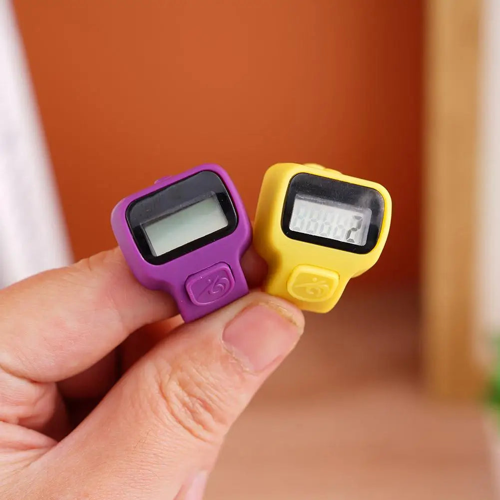 A hand holds a purple and yellow digital tally counter device displaying the number 2.