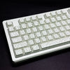 A close-up view of a white mechanical keyboard with side-lit keycaps resting on a dark surface.