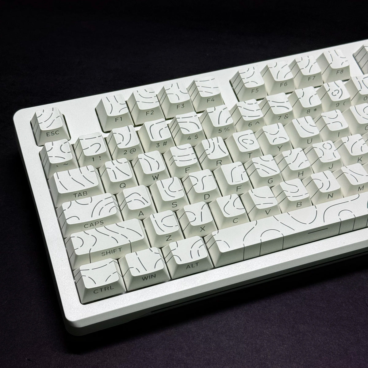 A close-up view of a white mechanical keyboard with side-lit keycaps resting on a dark surface.