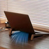 Ein braunes Laptop ruht auf einem verstellbaren Holzständer auf einem Holzschreibtisch, beleuchtet durch Sonnenlicht durch Ja