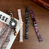 A close-up of a black watch with a gold-toned resin beaded watch band and a matching watch face, displayed on a wooden surfac