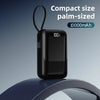Batterie portable noire de la taille d'une paume avec indicateur de batterie et boucle flexible, sur une surface bleue.