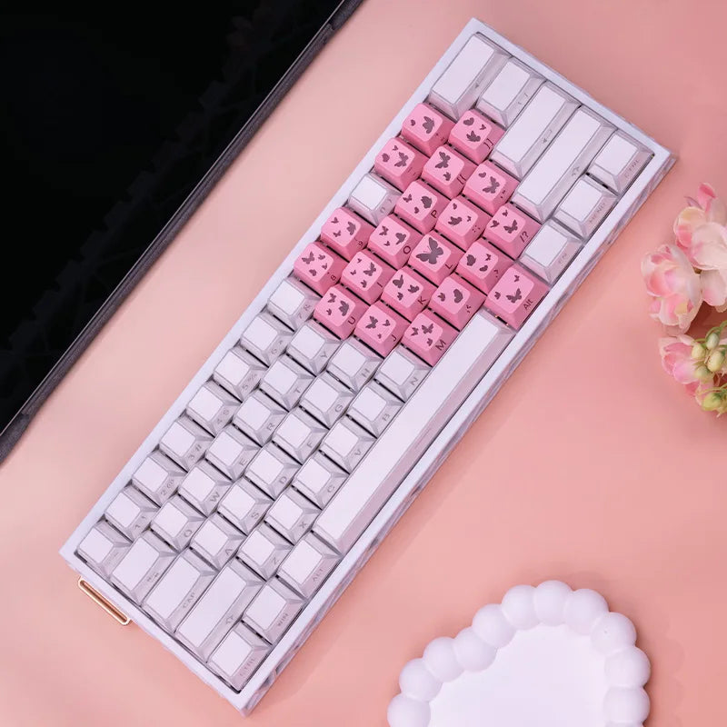 Nahaufnahme einer weißen mechanischen Tastatur mit rosa Schmetterlings-Tastenkappen auf einer hellrosa Oberfläche.