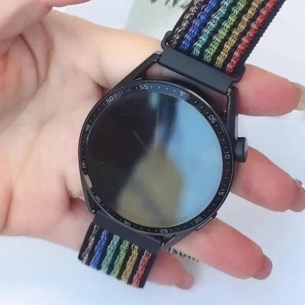 A close-up of a black digital watch with a multi-colored nylon loop strap being held in a person's hand.