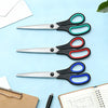 A set of three stainless steel scissors in black and colored handles resting on a light blue surface next to paper and a note