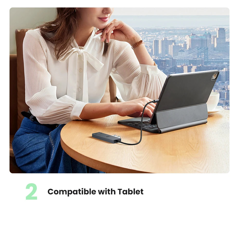 A woman is using a black tablet connected to a USB-C hub on a wooden table.