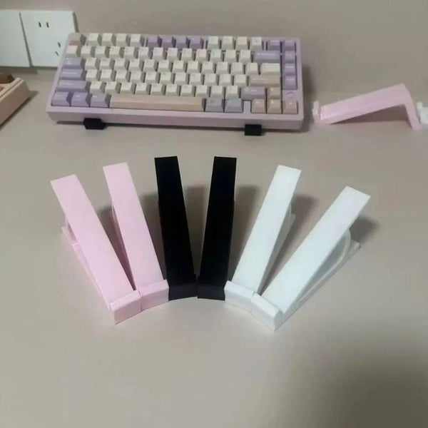 A collection of pink and white ergonomic keyboard height adjuster stands and a purple mechanical keyboard.