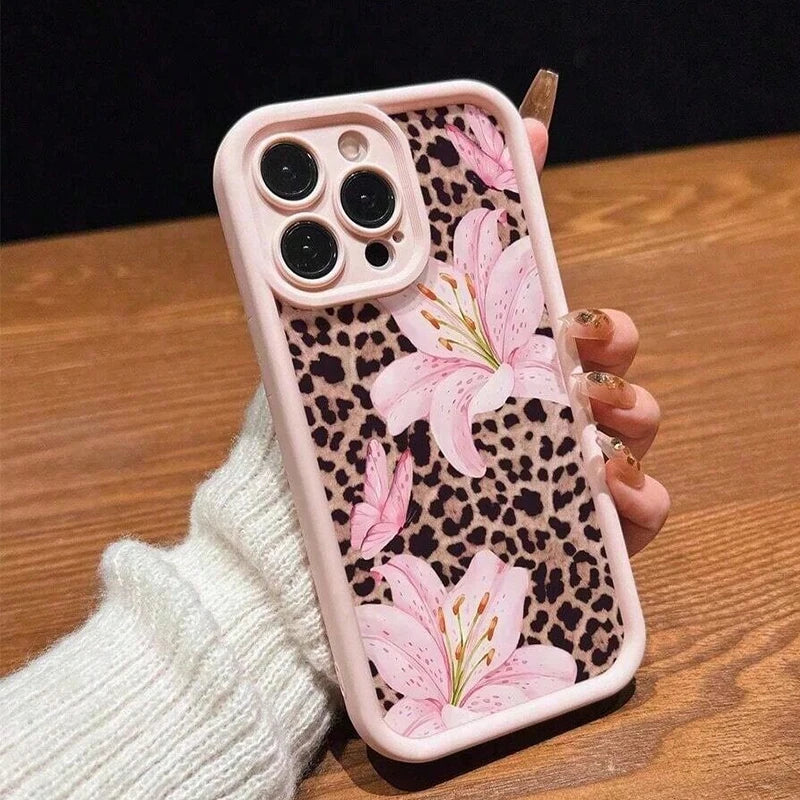 A pink leopard print phone case featuring a floral design is held in a hand on a wooden surface.