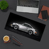 A silver JDM car is displayed on a black mouse pad next to a laptop and writing tools.