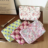 A collection of floral quilted ladies clutch purses in various pink, green, and purple patterns are displayed on a wooden sur