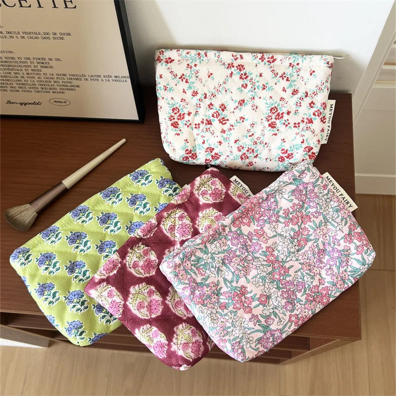 A collection of floral quilted ladies clutch purses in various pink, green, and purple patterns are displayed on a wooden sur