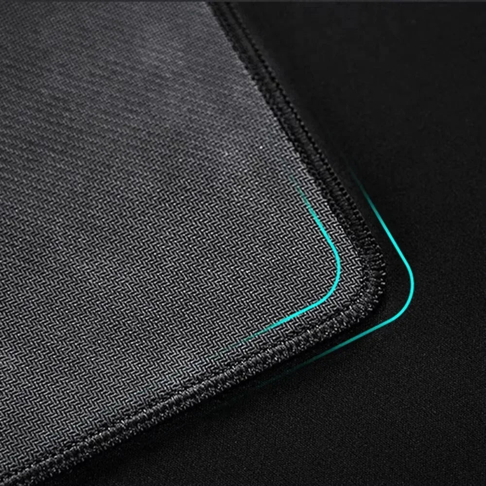 A close-up view of a gray overlocked mouse pad with a teal trim on a dark surface.