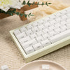 A close-up of white custom printed jelly keycaps for a mechanical keyboard resting on a beige fabric with a green leaf.