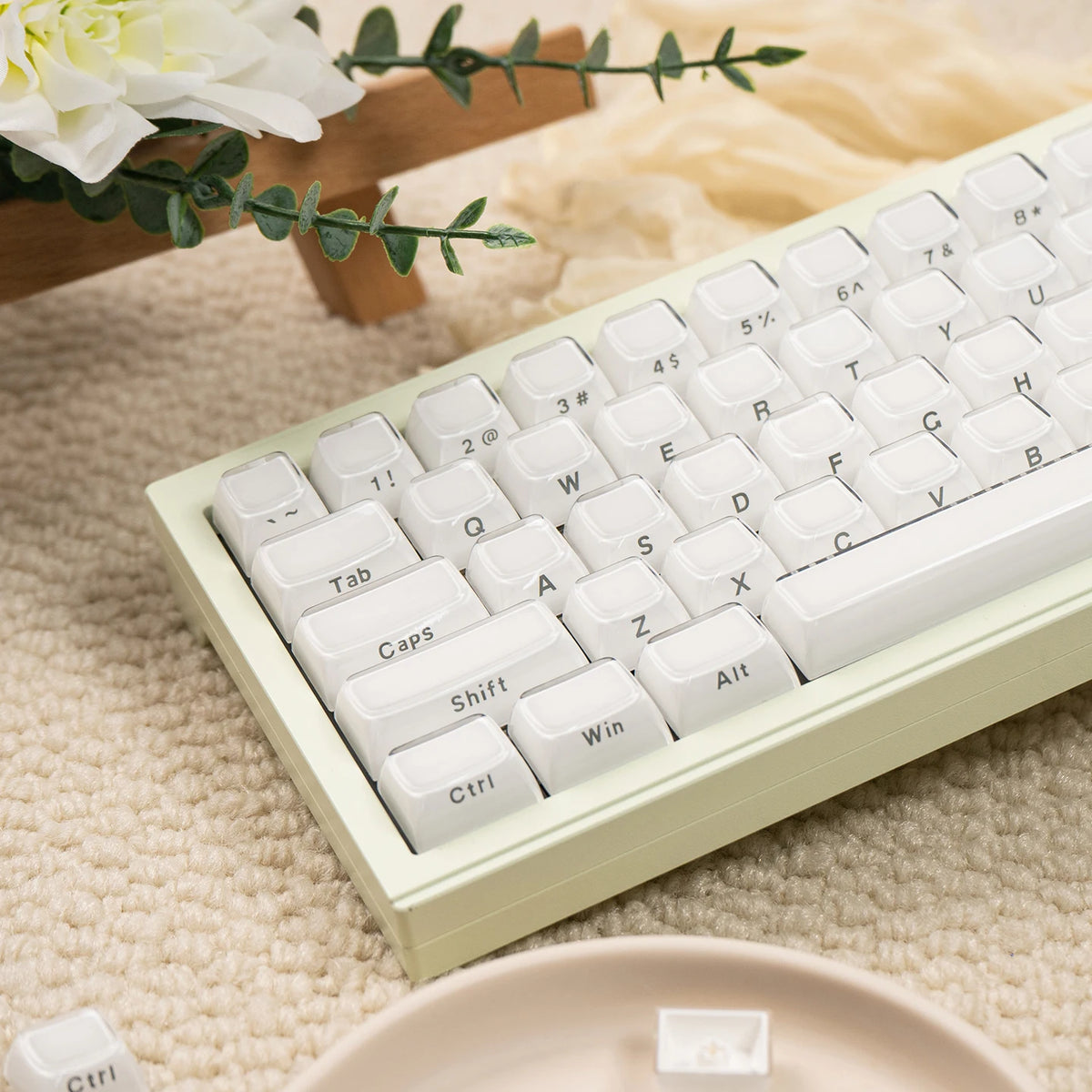 A close-up of white custom printed jelly keycaps for a mechanical keyboard resting on a beige fabric with a green leaf.