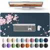 A large PU leather desk mat featuring a laptop and keyboard, surrounded by scattered pink cherry blossoms and various colored