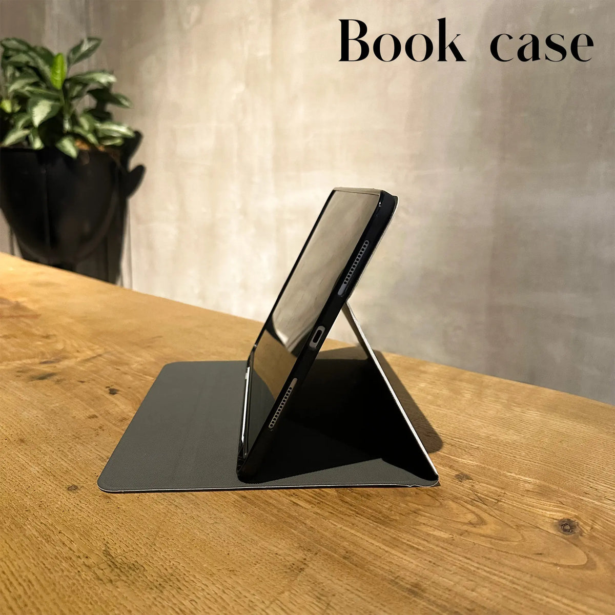 A black book case holding a smartphone on an angled stand, set on a wooden surface.