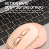 A pink wireless computer mouse is shown resting on a wooden surface next to a laptop keyboard.