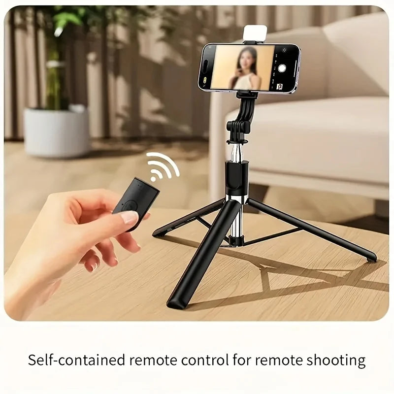 A hand holds a black wireless remote control for a professional extendable selfie stick tripod setup.