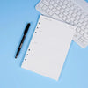 Una página de cuaderno de planificación semanal junto a un bolígrafo negro y un teclado de laptop blanco sobre un fondo azul 