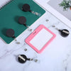 A pink badge reel is displayed next to a green notepad and several retractable badge reels with crocodile clips.