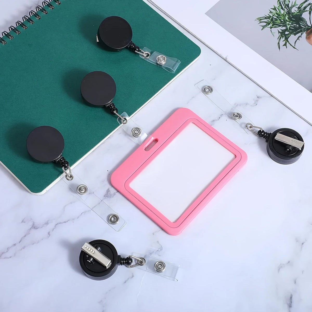 A pink badge reel is displayed next to a green notepad and several retractable badge reels with crocodile clips.