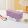 A lavender pencil case with a gold zipper lies on a white surface next to makeup brushes.