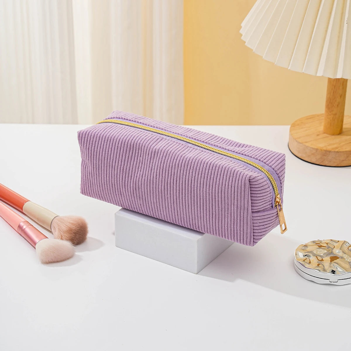 A lavender pencil case with a gold zipper lies on a white surface next to makeup brushes.