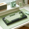 A close-up view of a dark green MOA Profile PBT keycaps set for mechanical keyboards resting on a light green surface.