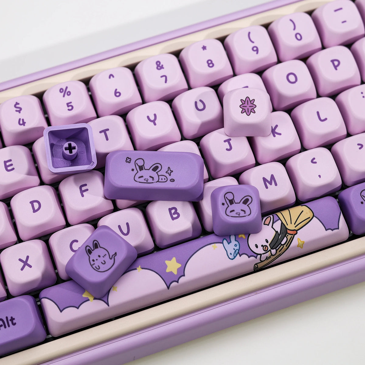 A close-up view of a purple Magic Bunny PBT keycap set with various characters and symbols on a light pink keyboard tray.