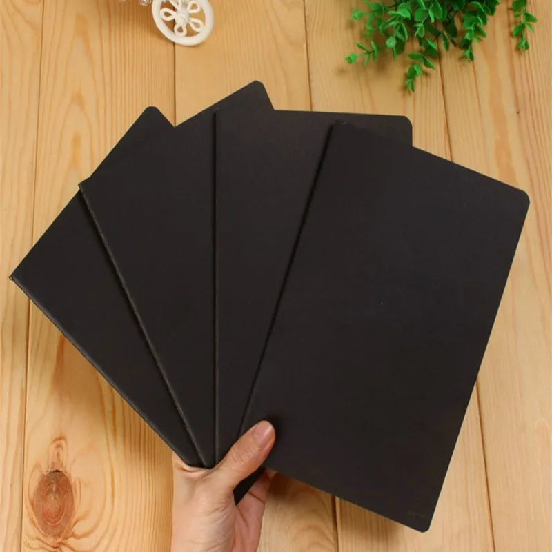 A stack of black A6 blank sketchbooks for art and journaling being held by a hand on a wooden surface.