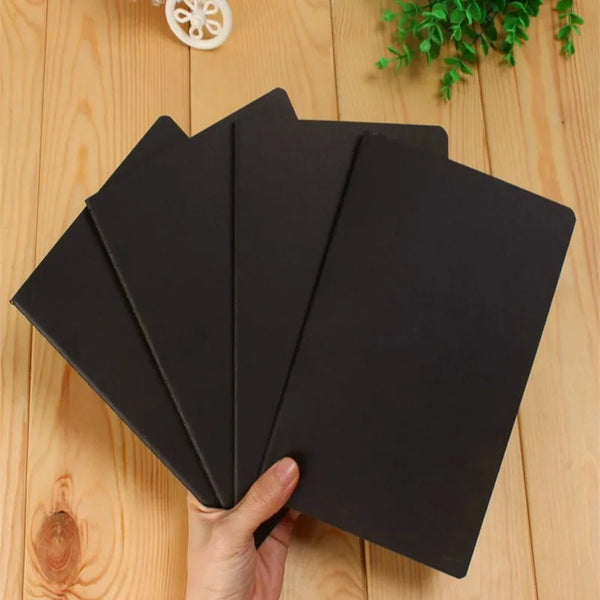 Ein Stapel schwarzer A6 leerer Skizzenbücher für Kunst und Tagebuchführung, gehalten von einer Hand auf einer Holzoberfläche.