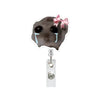 A black hamster face acrylic badge reel featuring teary eyes and a pink bow.