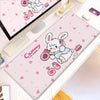 A pink cartoon gaming desk mat featuring a white rabbit illustration and pink accessories.