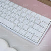 A close-up view of a white mechanical keyboard with translucent keycaps resting on a pink surface.