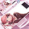 A close-up of a person with pink hair lying on a pink desk mat next to a computer and various stationery items.
